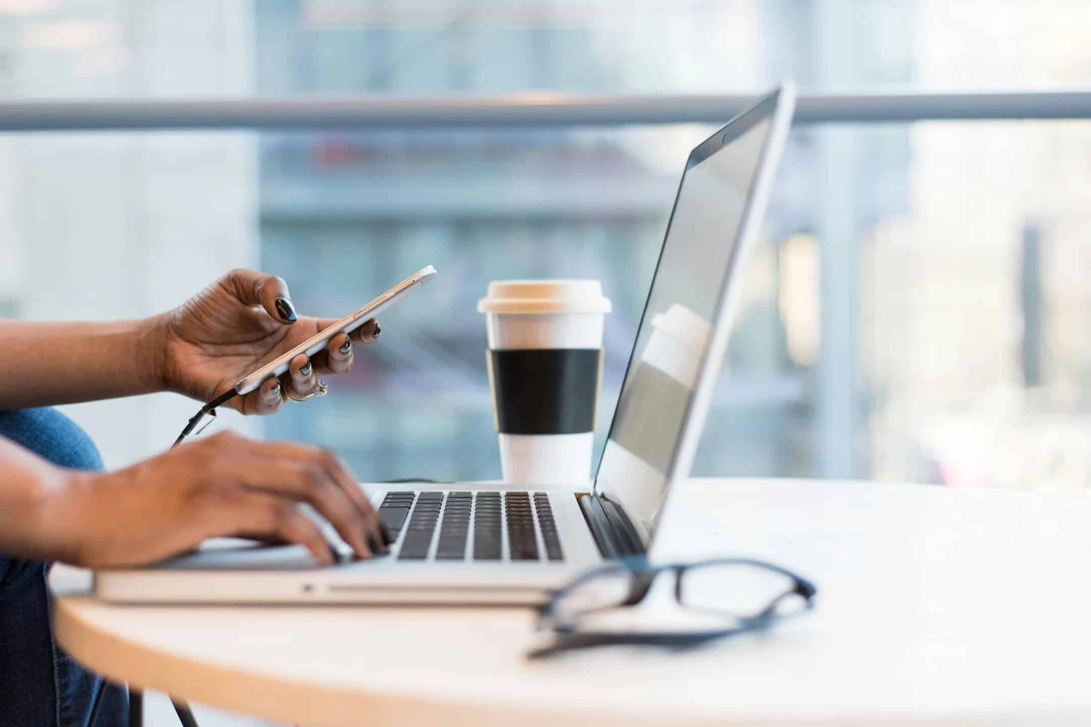 Woman's hand holding a phone in front of a laptop